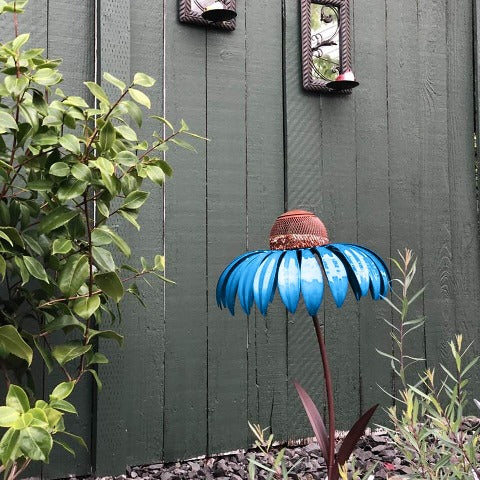 Blue Garden Petal Shape Bird Feeder in a garden next to a green fence